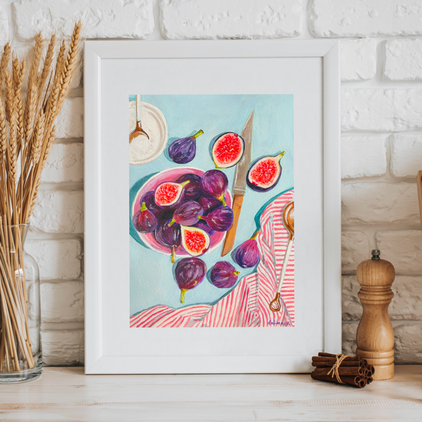 Framed artwork of figs on a kitchen counter with a white brick wall background