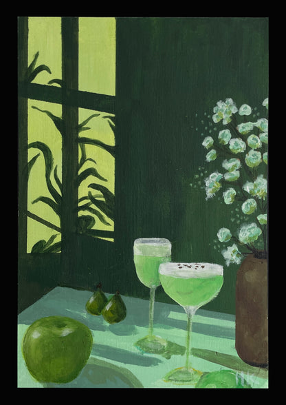 Two green cocktails on a table with a window and plant in the background
