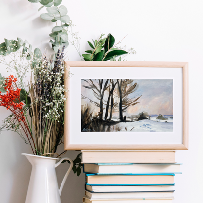 Framed winter landscape print on a stack of books with a vase of flowers.