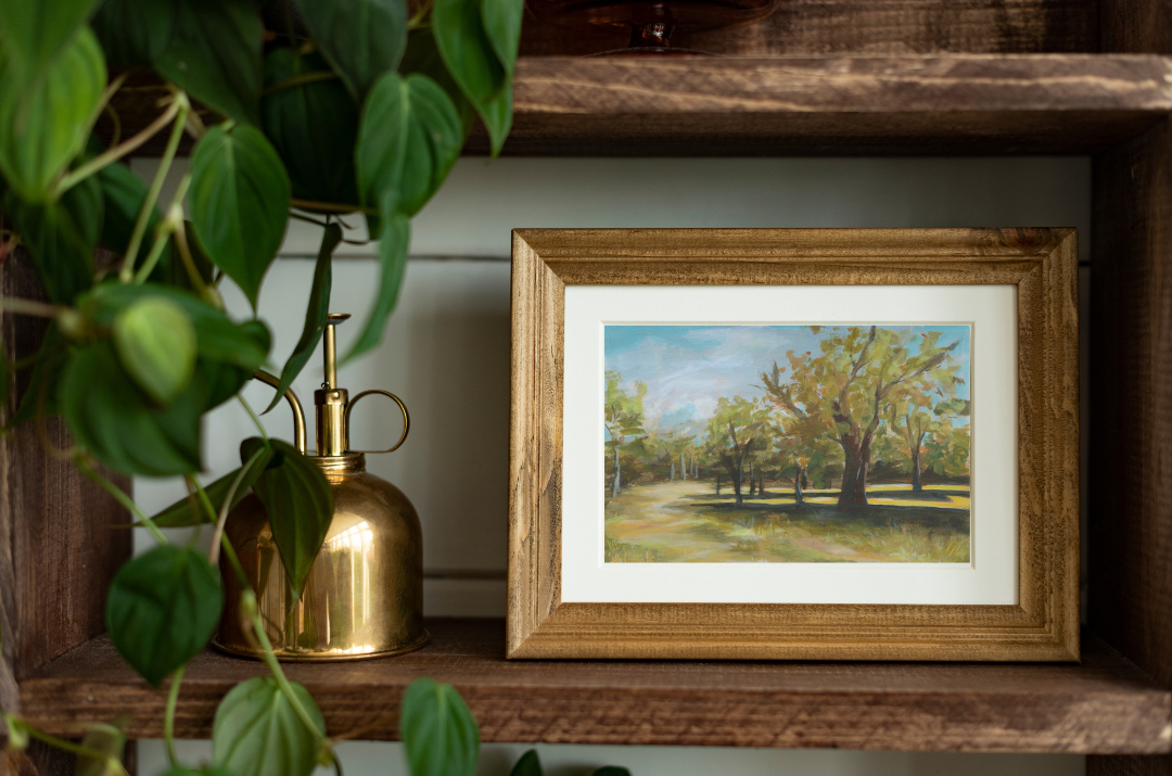 Halima Khanum's Greenwich Park Landscape Painting in antique gold frame on wooden shelf with mister and leaves