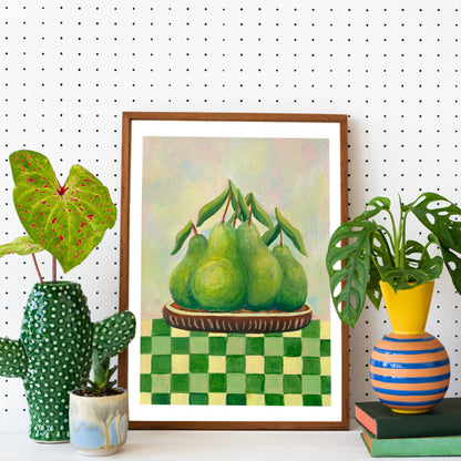 Framed artwork of pears on a checkered tablecloth with decorative plants and books in the foreground.