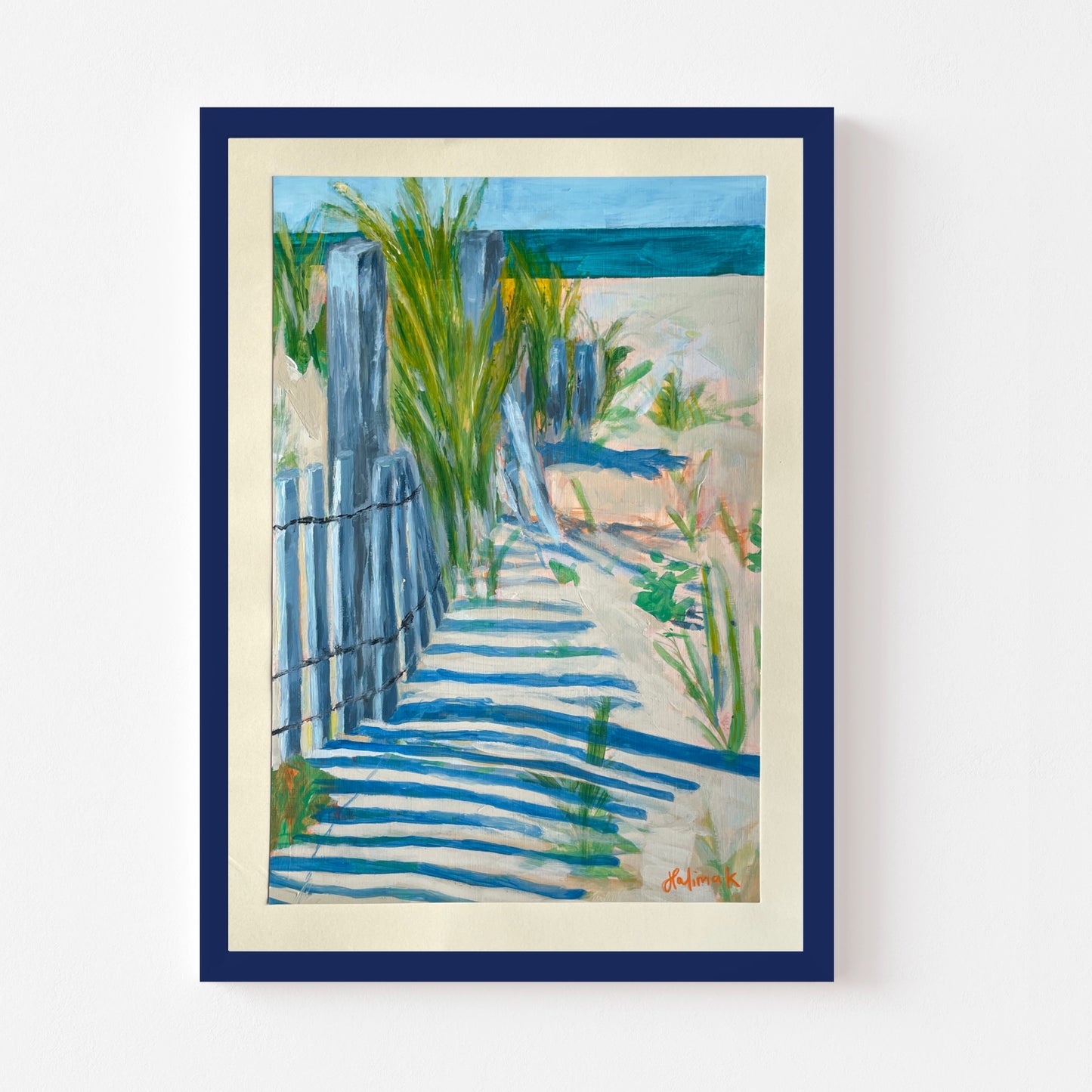 Framed artwork of a beach scene with a blue fence and greenery.