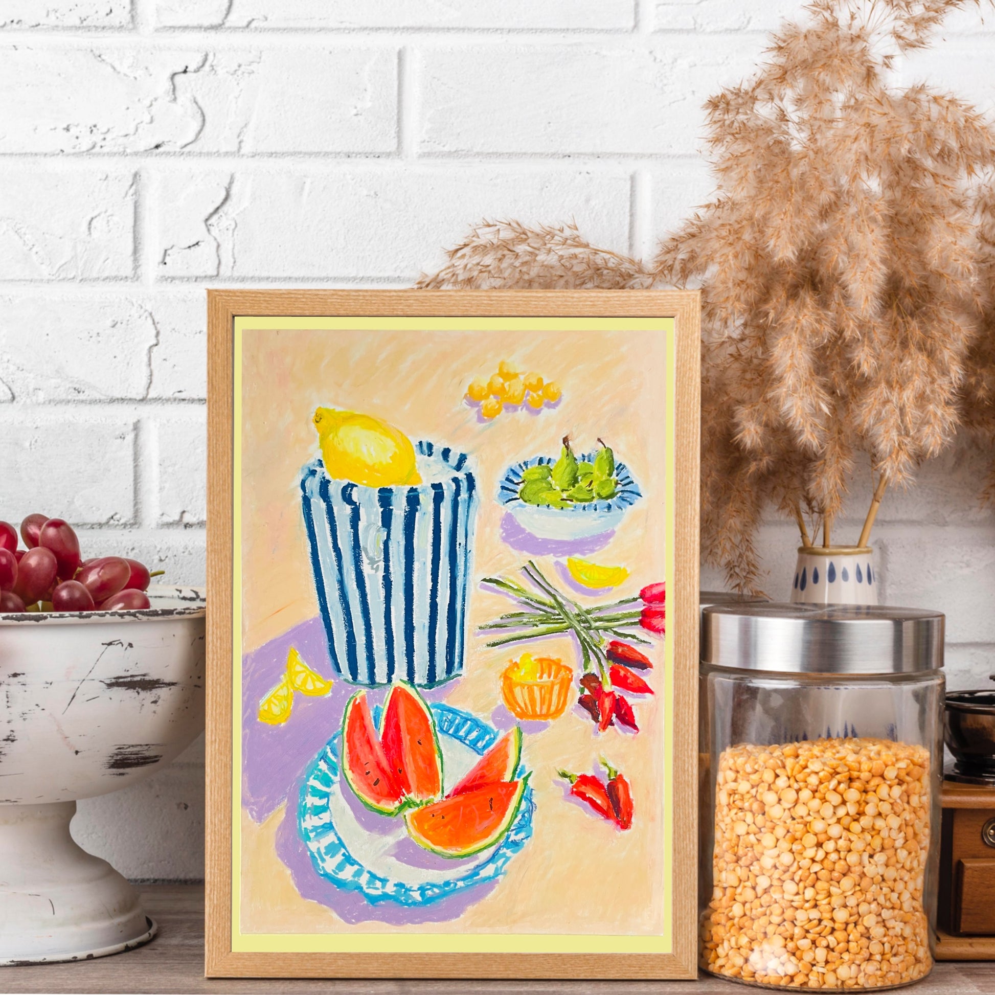 Framed artwork of a still life with fruits and vegetables on a table, against a white brick wall.