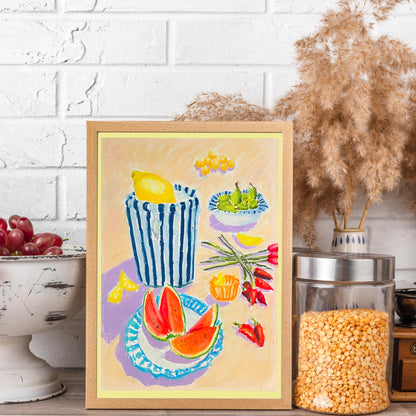 Framed artwork of a still life with fruits and vegetables on a table, against a white brick wall.