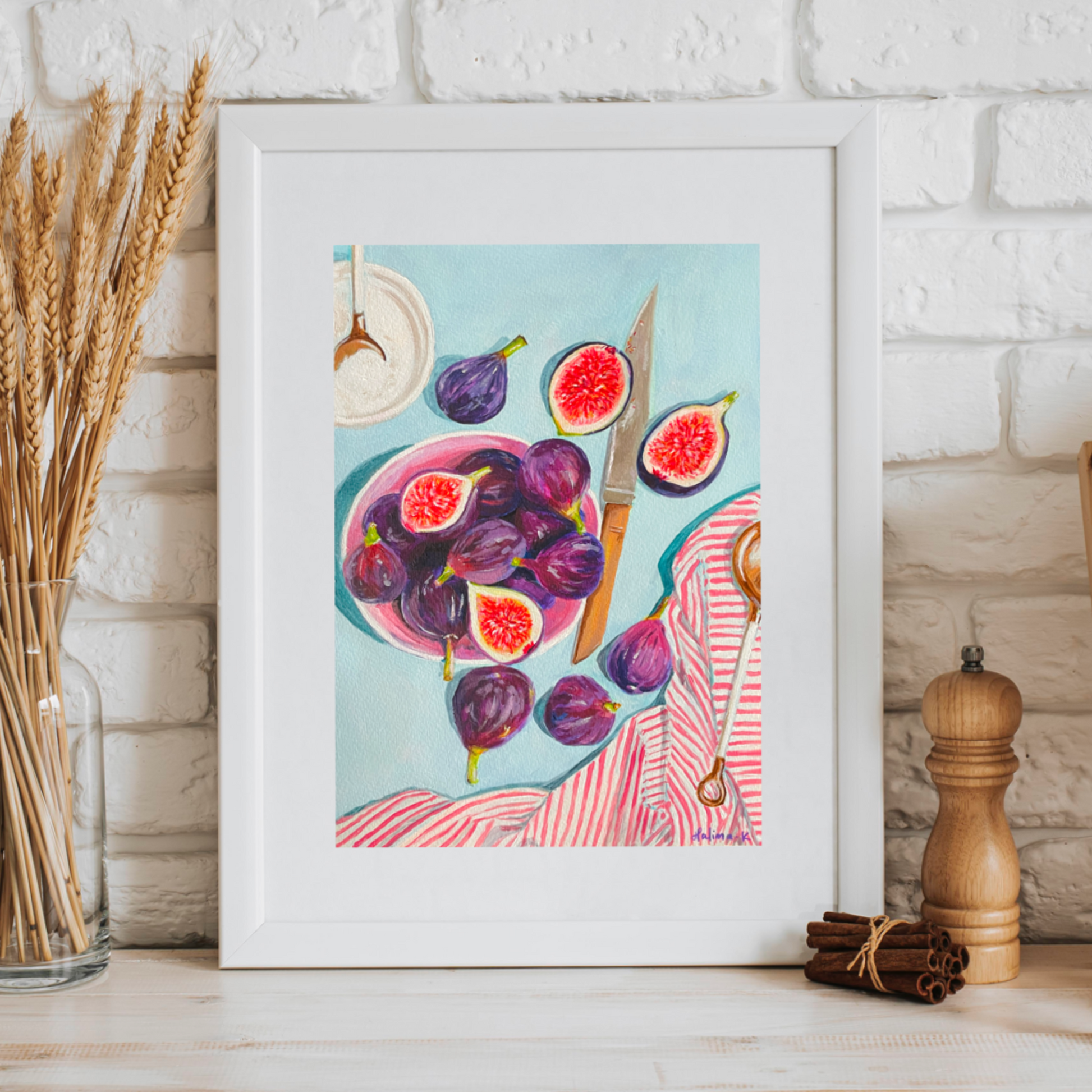 Framed artwork of figs on a kitchen counter with a white brick wall background