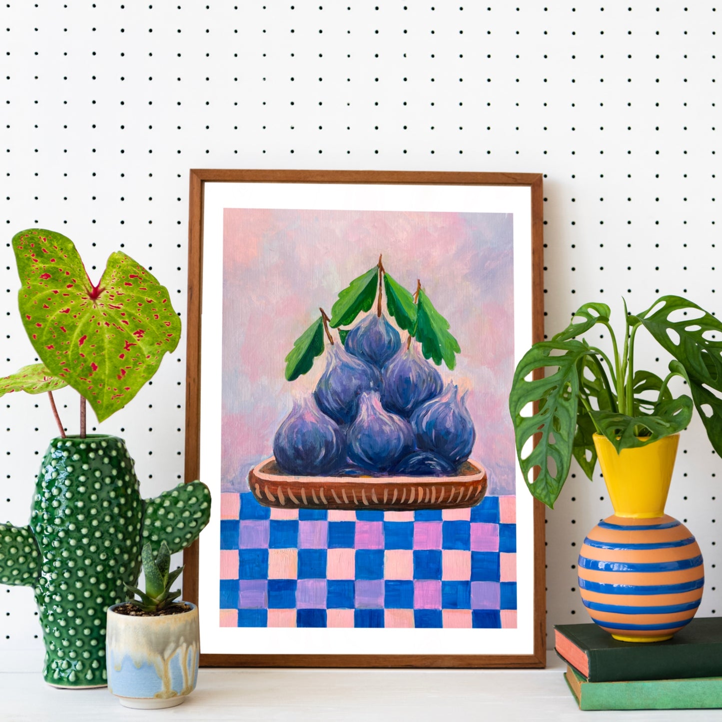 Framed artwork of purple fruits on a checkered background, surrounded by decorative plants and vases.